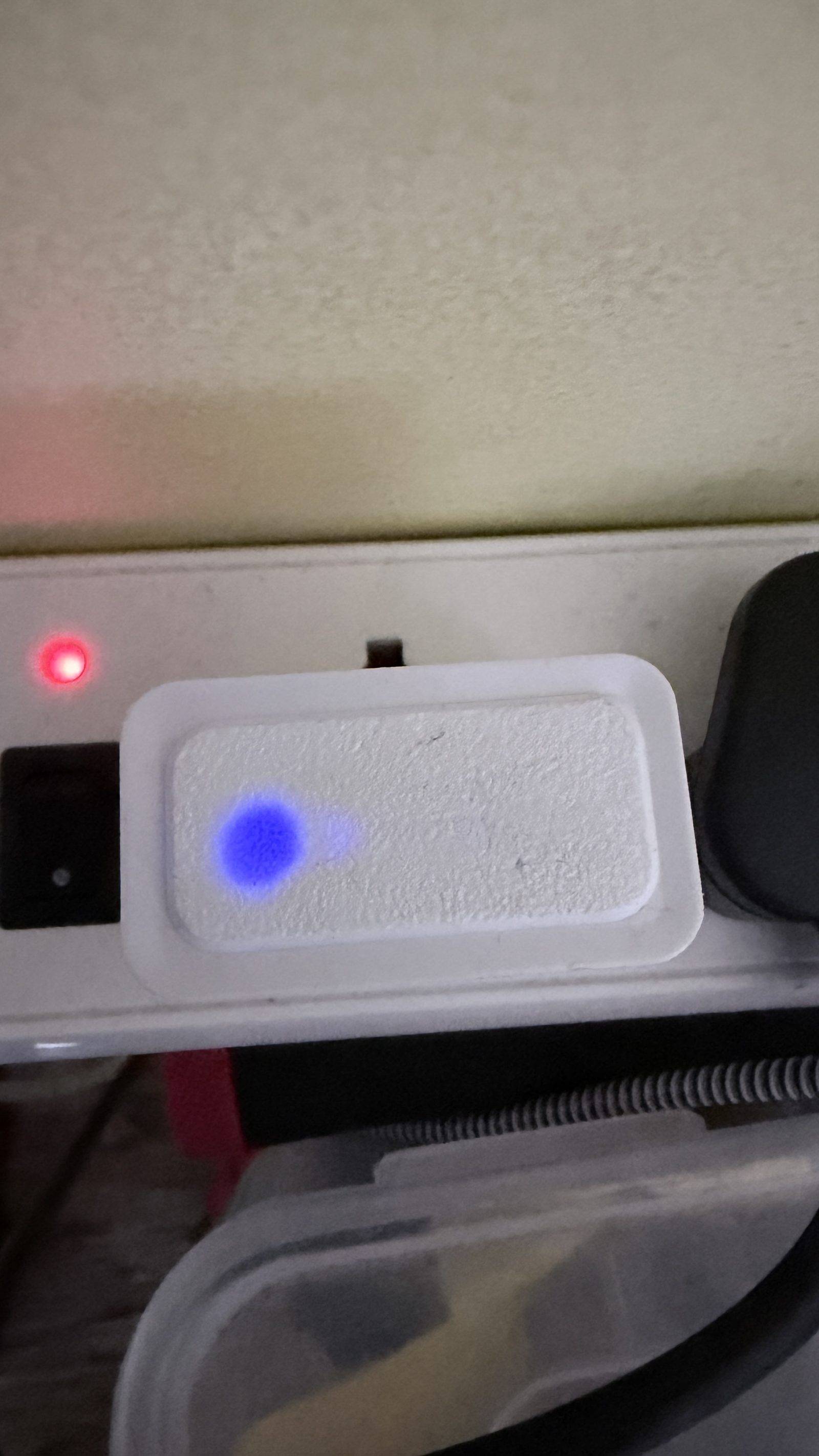 The Aura Core plugged into an outlet, with its blue LED glowing through the front plate.